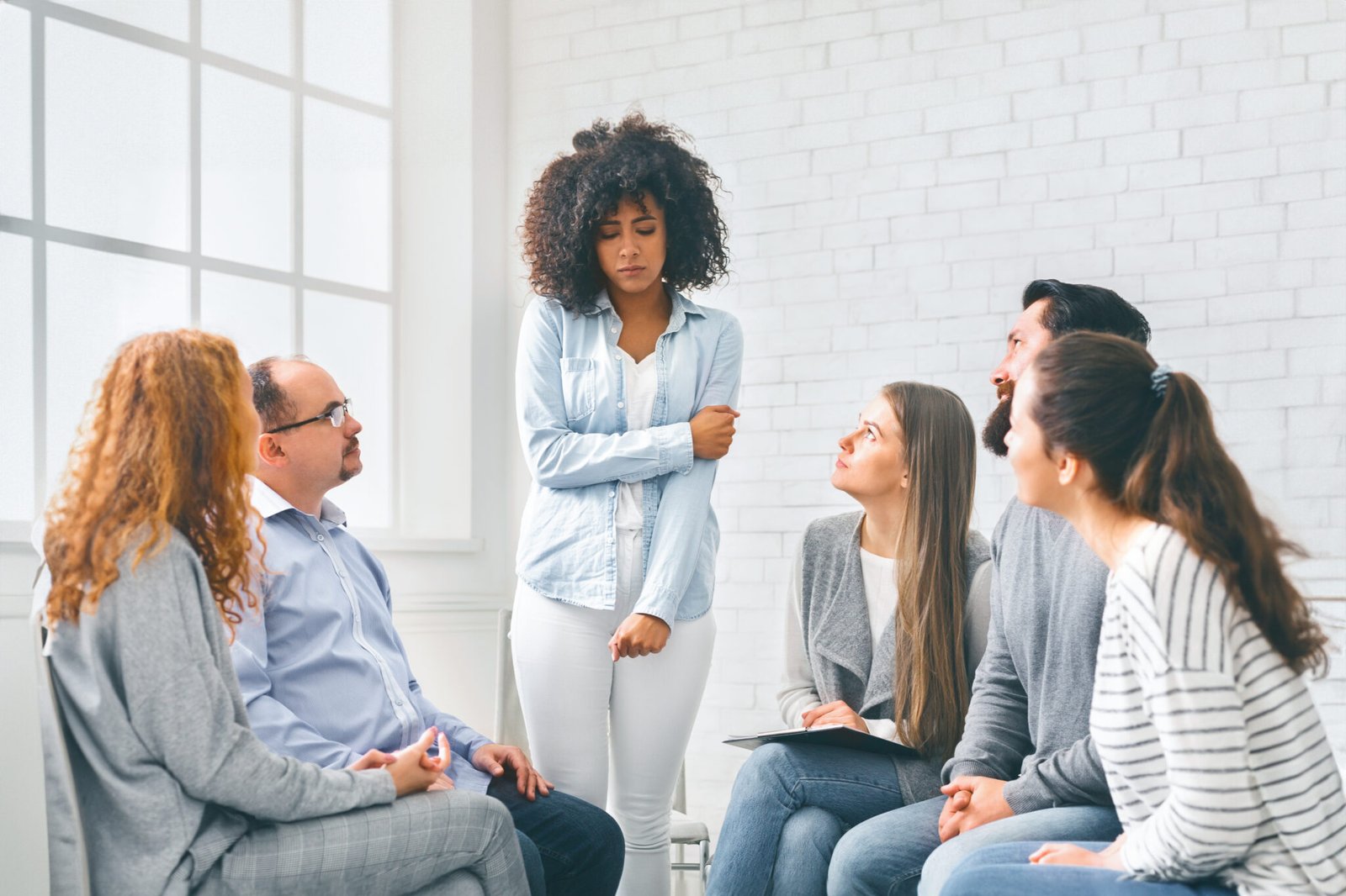 Rehab group listening to stressed woman standing up introducing herself at therapy session, free space